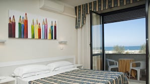 A hotel room with a bed, a painting of colored pencils, a balcony with chairs, and a view of the sea. - Hotel Genzianella (Cervia)