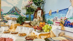 A buffet with various food items, a decorative plant, and a mural depicting a coastal scene. - Hotel Genzianella (Cervia)