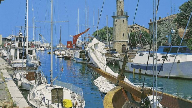 A marina with multiple boats docked, a lighthouse, and a building with a tower. - Hotel Genzianella (Cervia)
