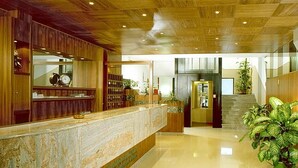 A reception area with a marble counter, wooden paneling, a clock, and a staircase leading to another floor. - Hotel Genzianella (Cervia)