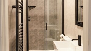 Un baño moderno con ducha de mampara de vidrio, un lavamanos blanco y un inodoro.