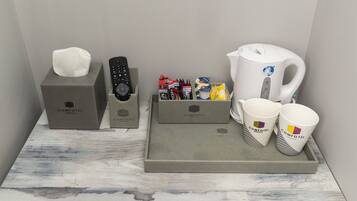 A hotel room's amenities tray with a tissue box, remote control, toiletries, and branded mugs.