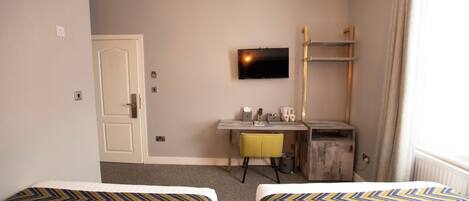 Habitación de hotel con dos camas, un escritorio, televisor y ventana con cortinas.