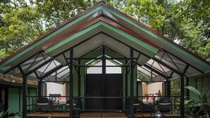Un edificio de dos pisos con fachada verde y techo de cristal. La planta baja tiene un área de estar con sillas y una mesa.