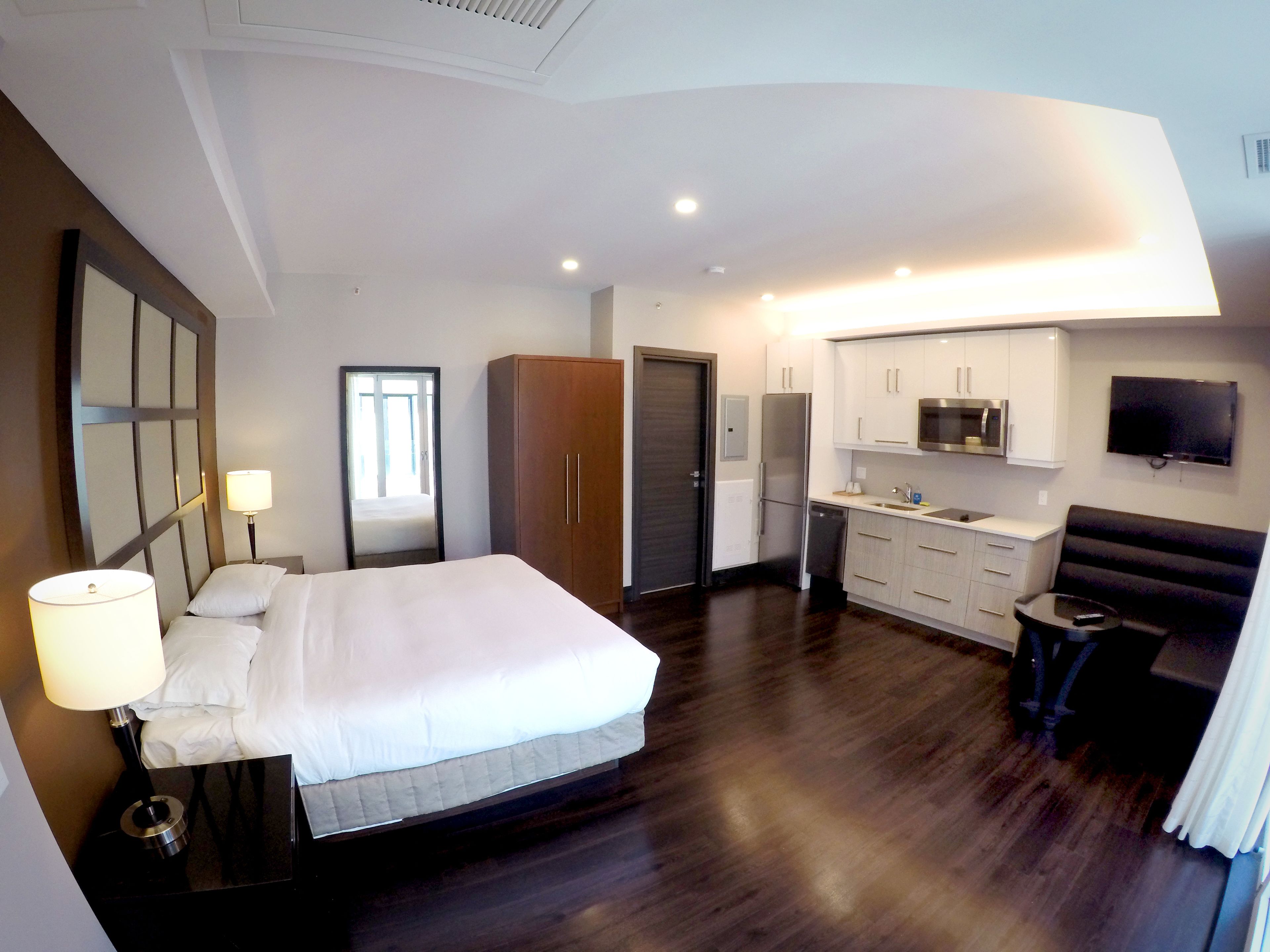 Ein modernes Hotelzimmer mit einem großen Bett, einem Schreibtisch, einem Kleiderschrank, einem Fernseher und einer Küchenzeile.