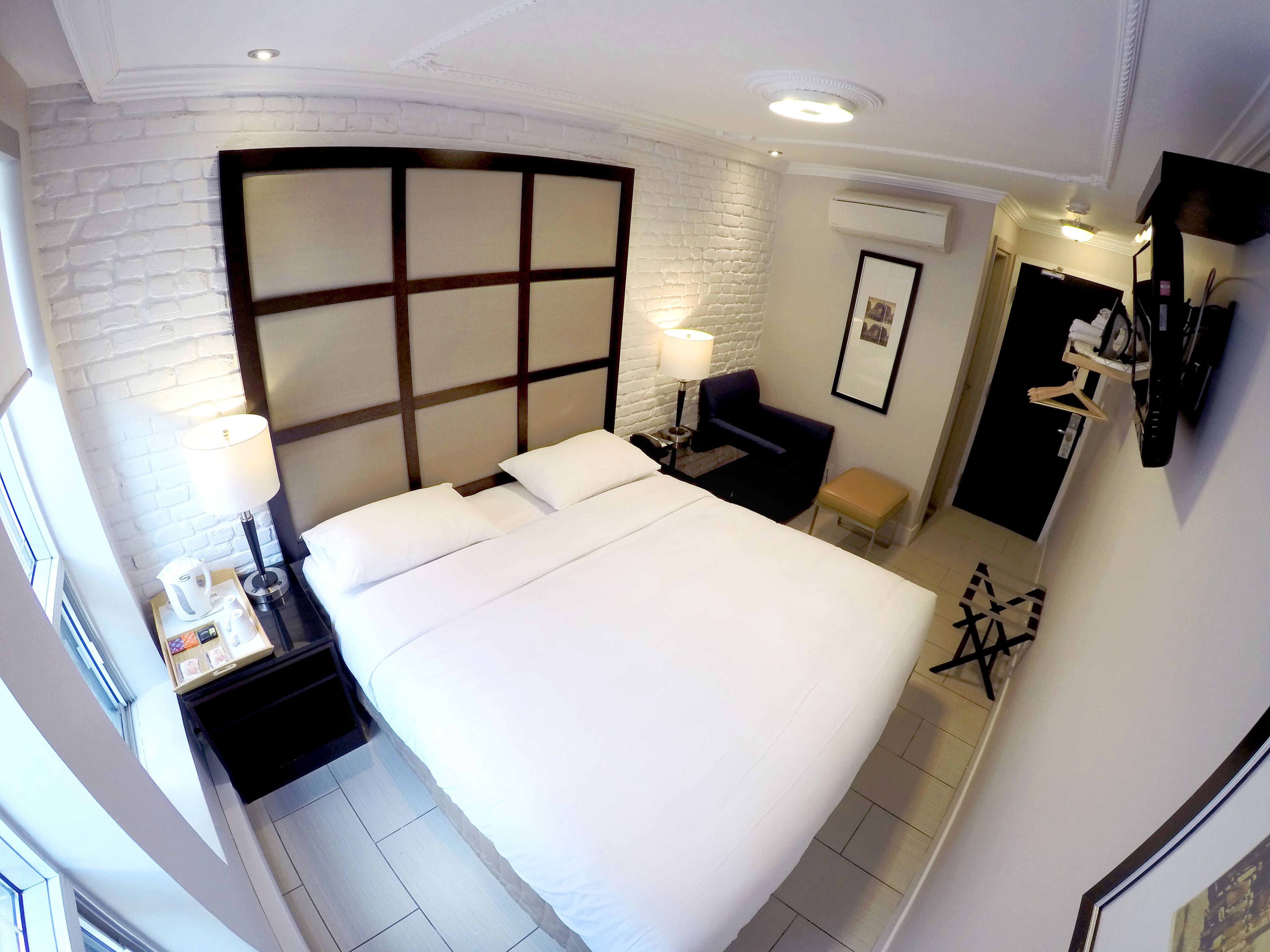 Een hotelkamer met een groot bed, nachtkastje met lamp, klein bureau, stoel en een kledingkast.
