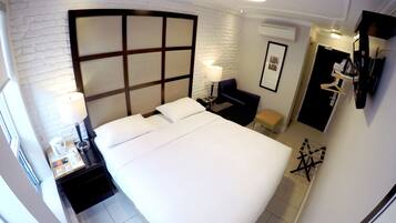 Een hotelkamer met een groot bed, nachtkastje met lamp, klein bureau, stoel en een kledingkast.