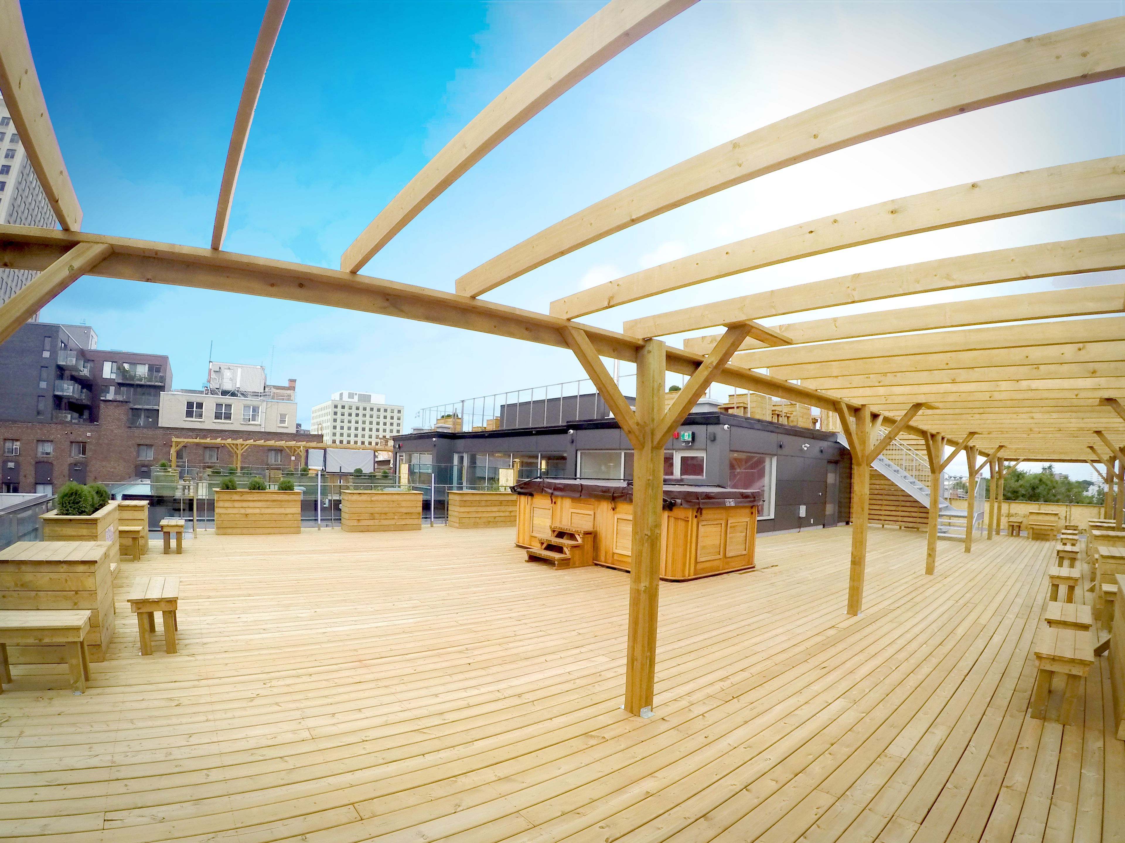 A wooden deck with seating and a bar area, overlooking a cityscape.
