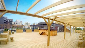 A wooden deck with seating and a bar area, overlooking a cityscape.
