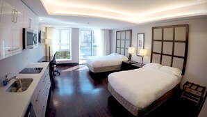 Ein Hotelzimmer mit zwei Betten, einem Schreibtisch mit Waschbecken und einem großen Fenster mit Blick nach draußen.