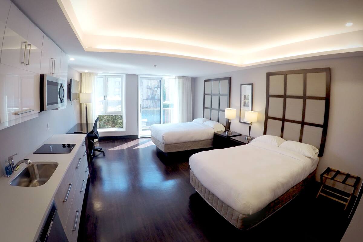 A hotel room with two beds, a desk with a sink, and a large window providing a view of the outside.