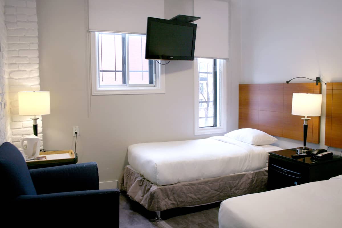 A hotel room with two beds, a television mounted on the wall, and two bedside lamps.