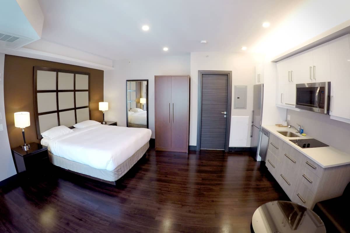 A modern hotel room with a large bed, a wardrobe, a mirror, a sink, and a microwave.