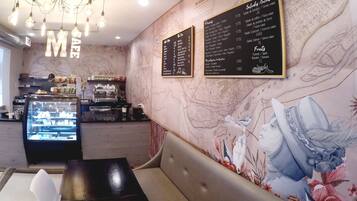L’intérieur d’un café, avec un mur en marbre, un tableau affichant le menu, un espace pour s’asseoir et une vitrine.