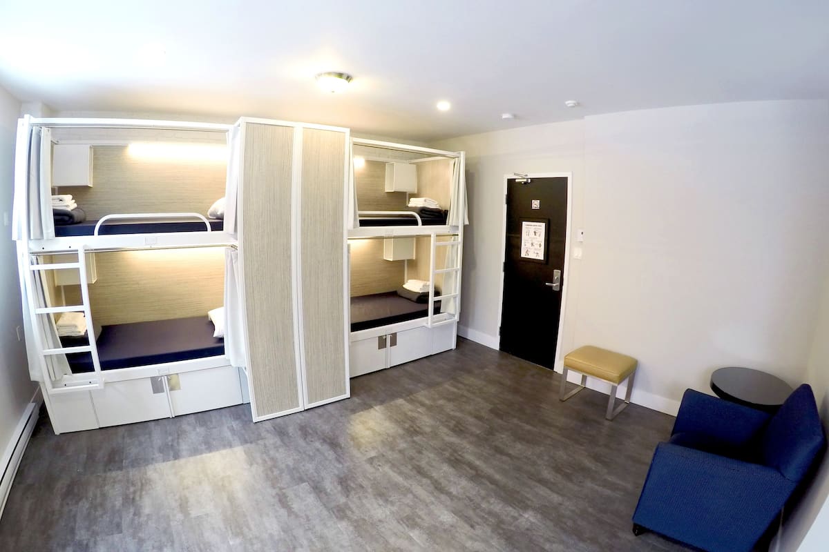 A room with bunk beds, a small bench, a round table, and a door with a sign.