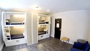 A room with bunk beds, a small bench, a round table, and a door with a sign.