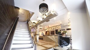 Ein moderner Hotel-Empfangsbereich mit einer Treppe zu den oberen Etagen, einem Empfangstresen und einer Kristallleuchter.