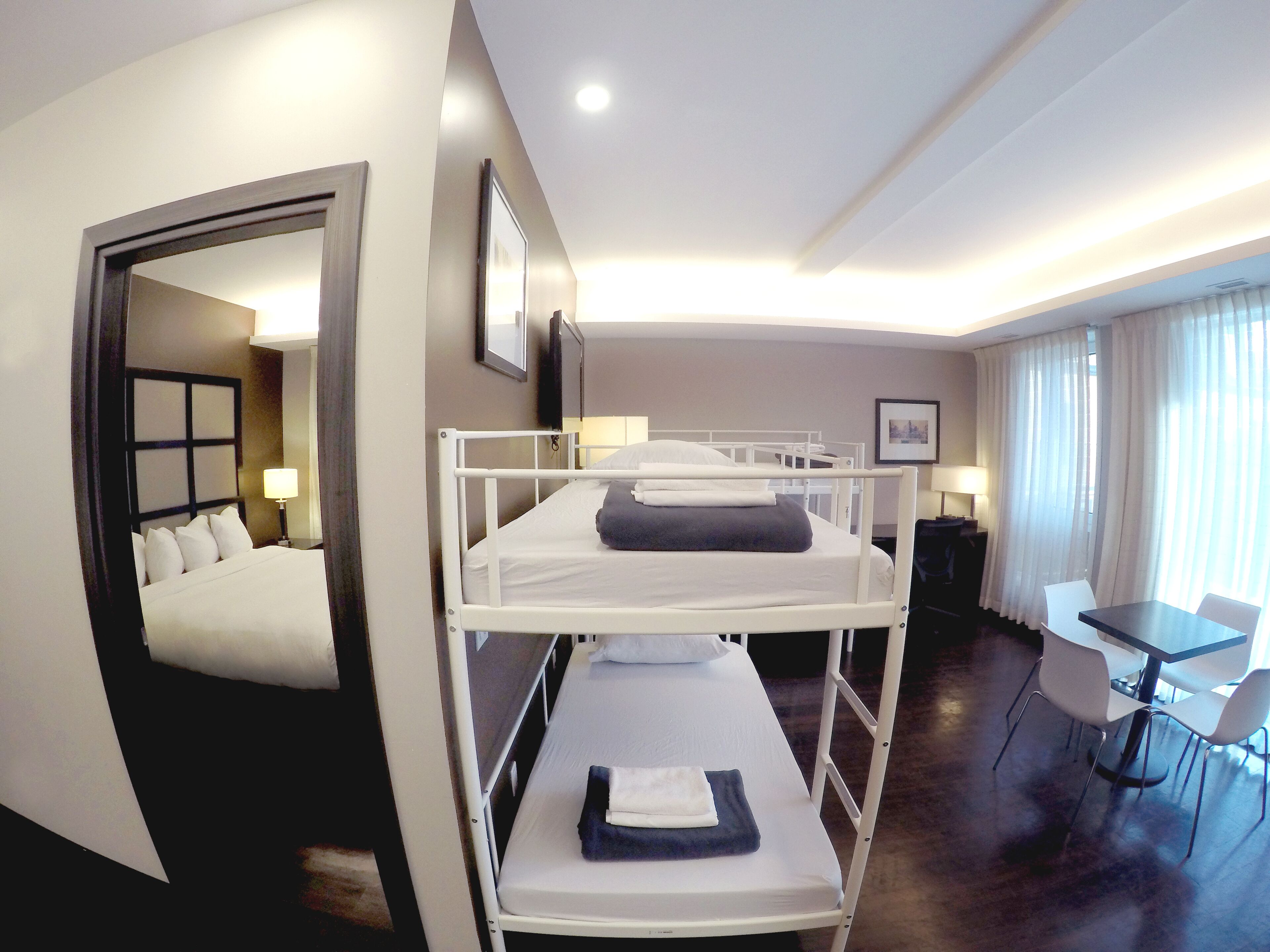 A hotel room with a bunk bed, a desk with a chair, and a dining area with a table and chairs.
