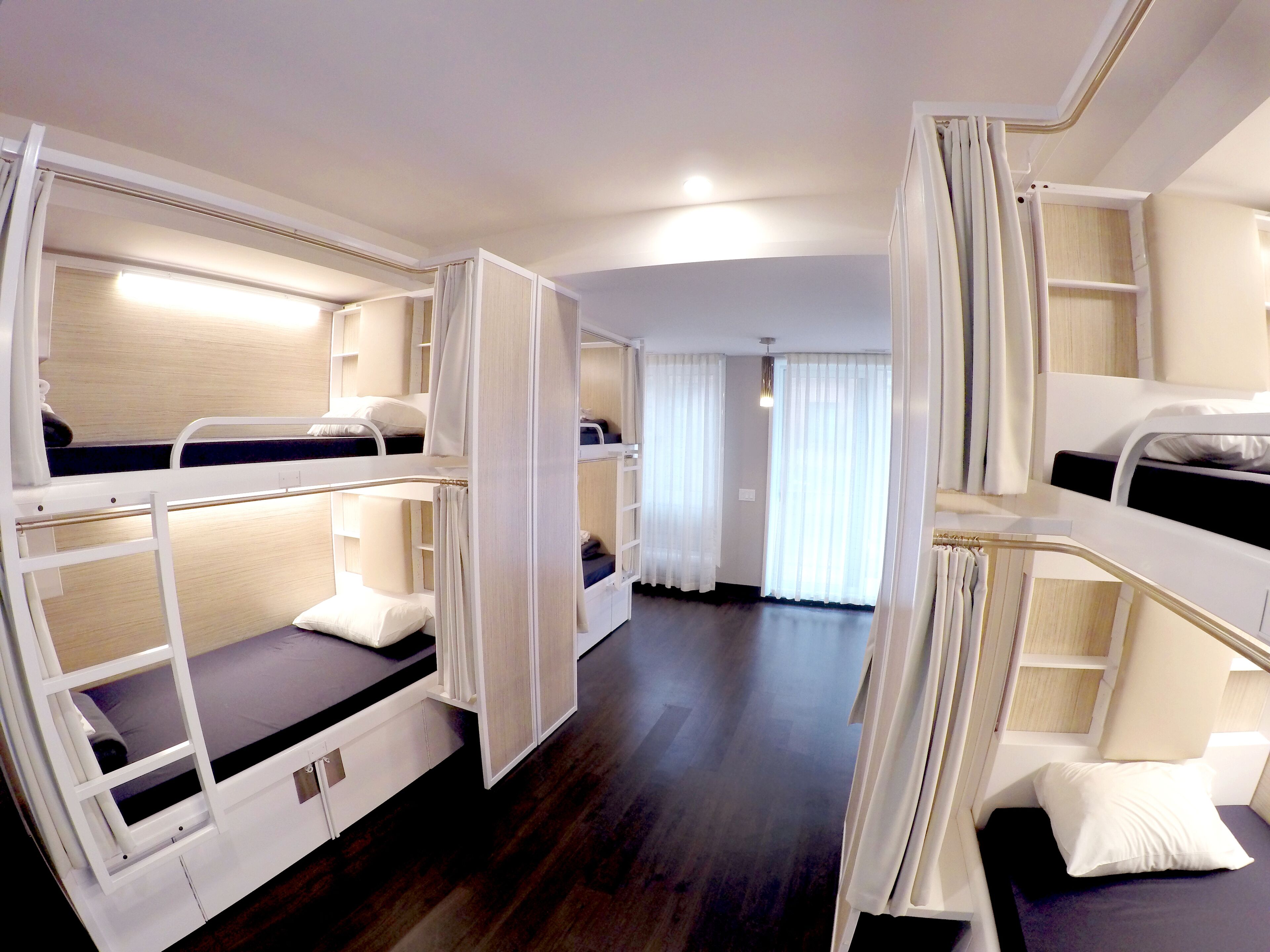 A hotel room with bunk beds, a wooden floor, and a view of the hallway.