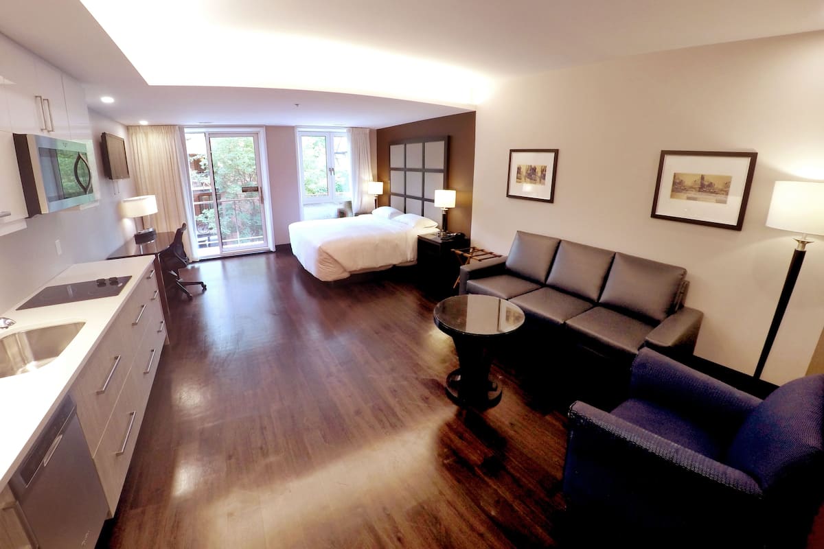 A modern hotel room with a bed, sofa, and a small dining table.