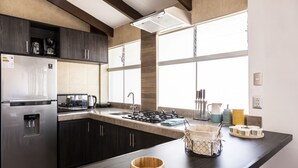 Une cuisine moderne avec des meubles de couleur sombre, un réfrigérateur en acier inoxydable, une cuisinière à gaz et une grande fenêtre qui laisse entrer la lumière naturelle.