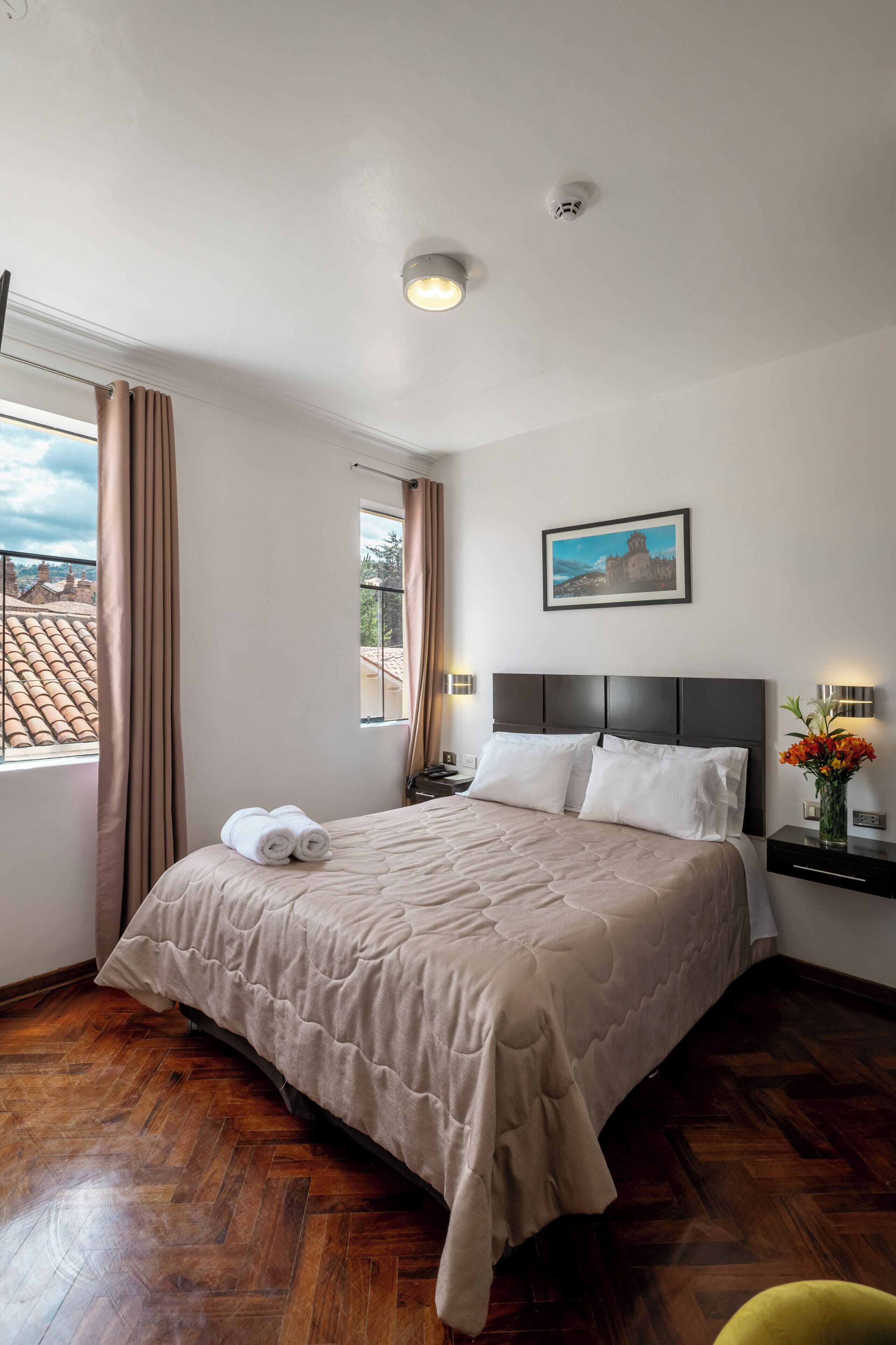 A hotel room with a large bed, a nightstand, a window with curtains, a wall-mounted picture, and a ceiling light.