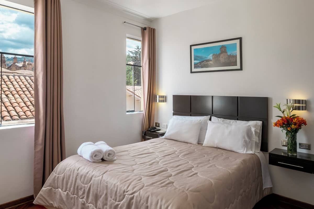 A hotel room with a large bed, a nightstand, a window with curtains, a wall-mounted picture, and a ceiling light.