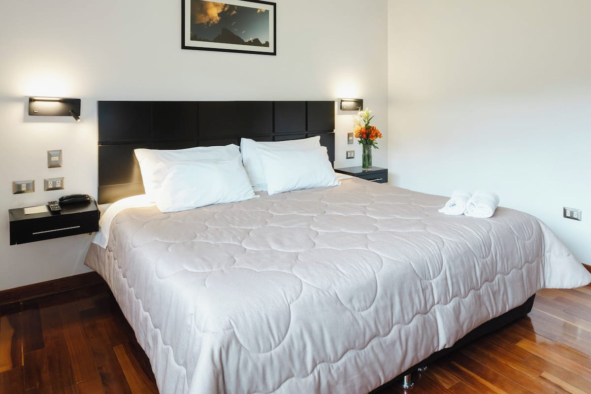 A bedroom with a bed, bedside tables, a nightstand, a wall-mounted light, and a framed picture.