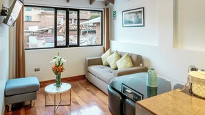 Un salon moderne avec un canapé, une petite table, un banc et une vue sur la ville grâce à de grandes fenêtres.