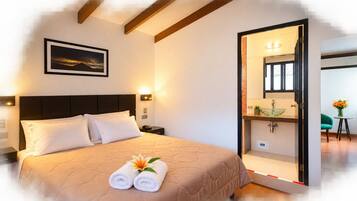 Habitación de hotel con cama, mesita de noche, lámpara de pared, un cuadro enmarcado y baño a la vista a través de una puerta abierta.