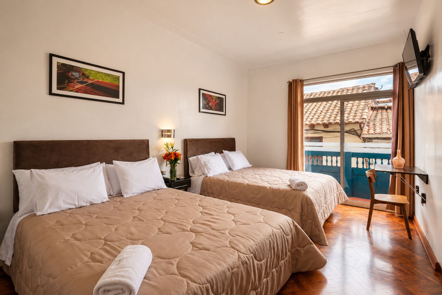 Une chambre d’hôtel avec deux lits, une petite table, une chaise, une fenêtre donnant sur un immeuble et des œuvres d’art accrochées aux murs.