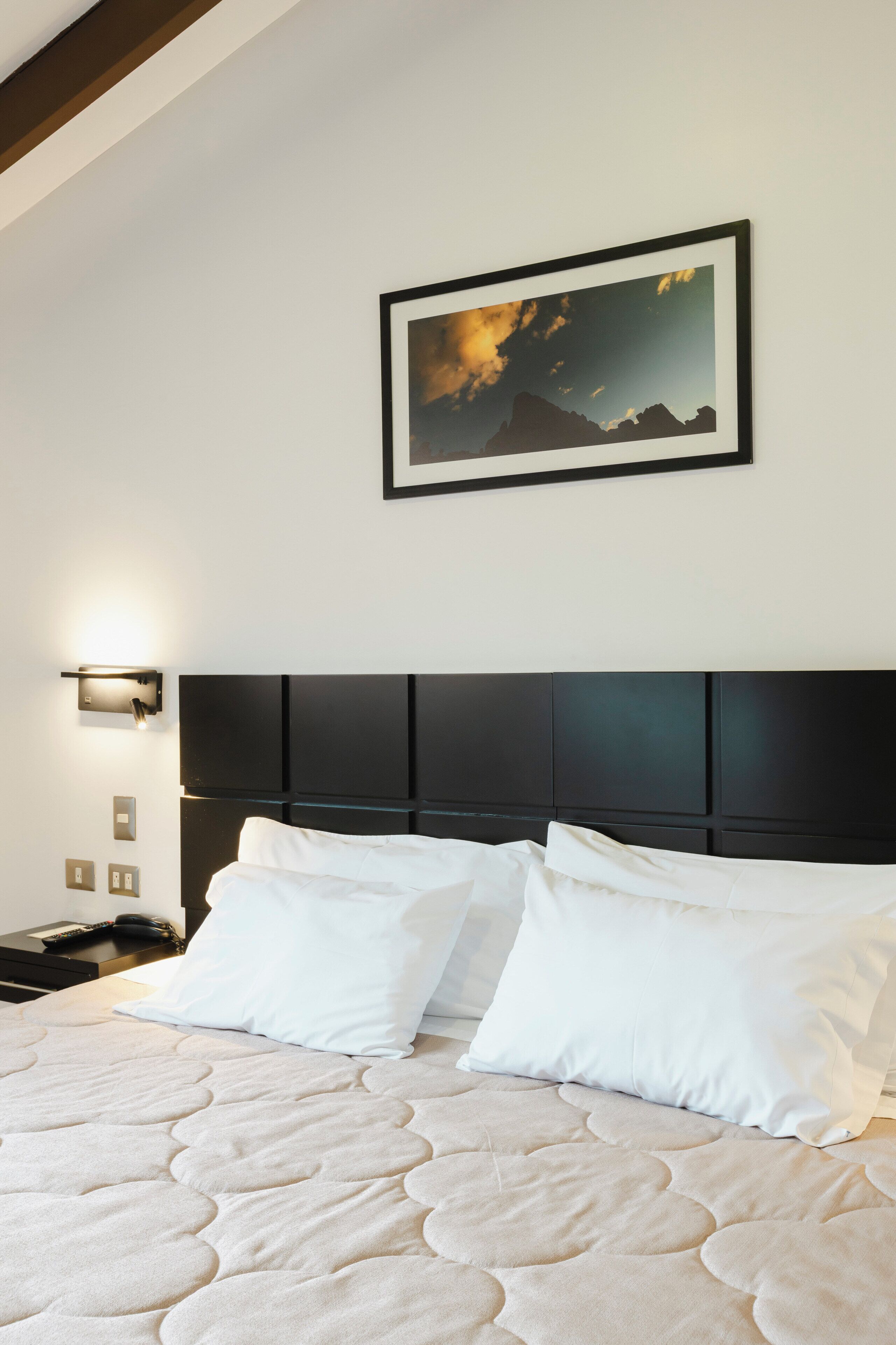 Un lit bien fait, avec une tête de lit matelassée, un tableau accroché au mur et une table de chevet avec une lampe.