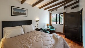 Une chambre d’hôtel avec un grand lit, un bureau, une chaise, une fenêtre donnant sur un beau paysage et une porte.