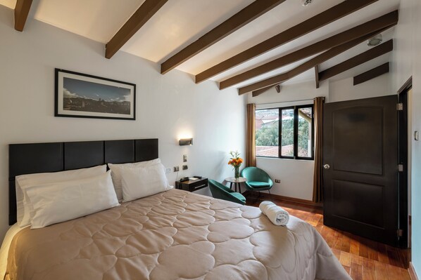 Habitación de hotel con una cama grande, un escritorio, una silla, un ventanal con vistas y una puerta.