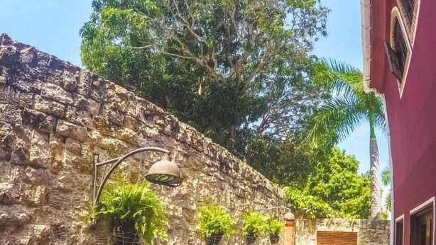 Piscina con paredes de piedra y macetas colgantes, rodeada por un edificio de fachada roja.