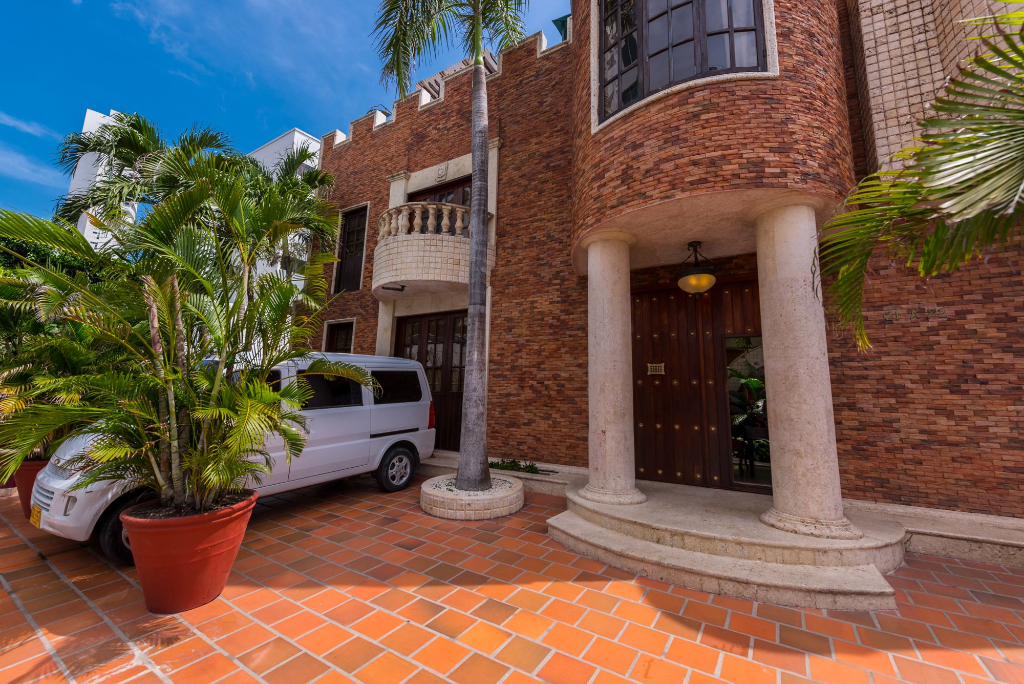A building with a brick facade, a white car parked in front, and a potted plant.