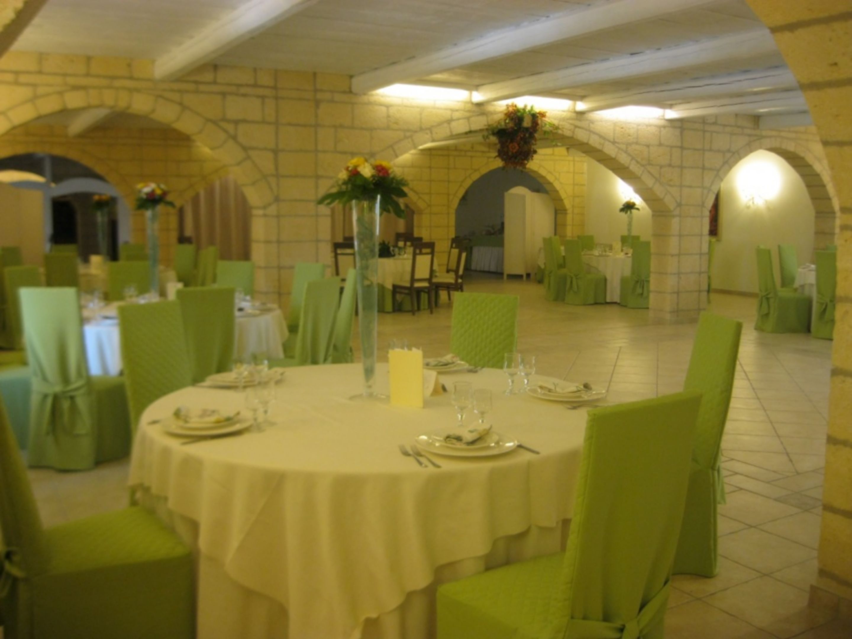 A dining area with round tables, green chairs, and white tablecloths.