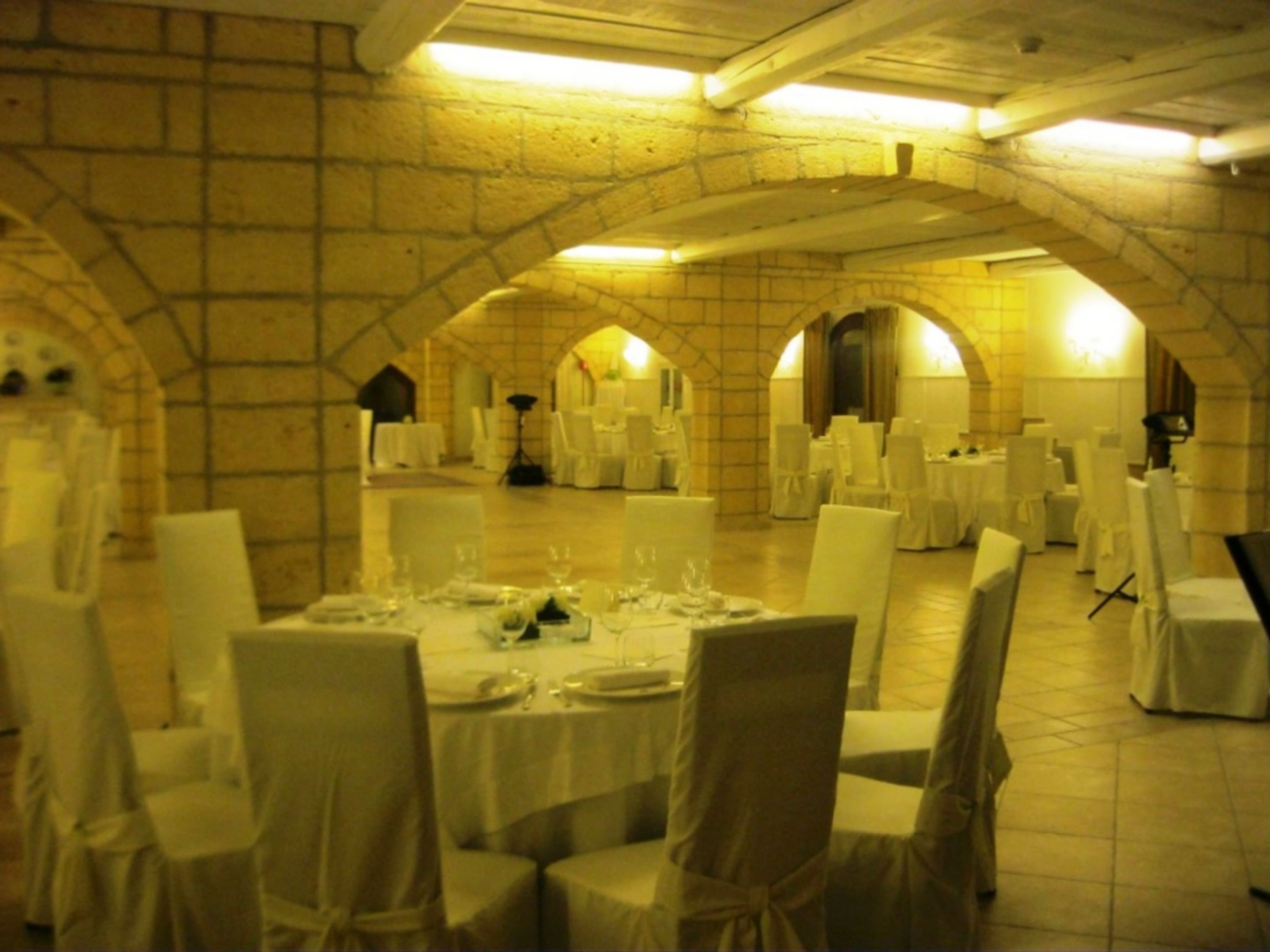 A banquet hall with tables set for a formal event, featuring arched brick walls and overhead lighting.