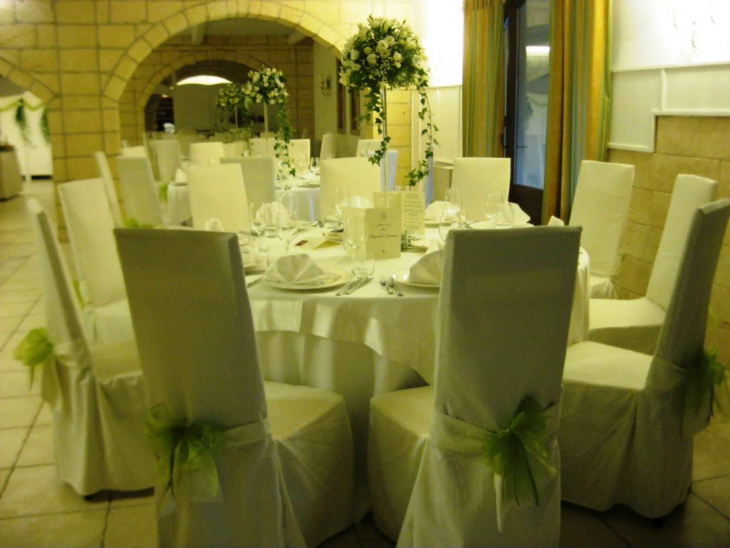 Une salle à manger élégante, avec des tables rondes, des chaises blanches et des centres de table floraux.