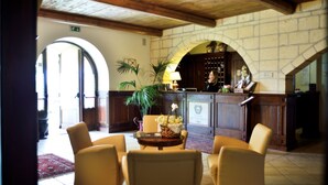 A lobby with a reception desk, a stone wall, and a large arched doorway. There are several chairs and a table with a vase of flowers. - Tenuta San Francesco (Trinitapoli)