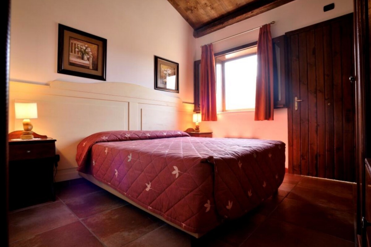 A bedroom with a bed, nightstands, a window with curtains, and wooden walls.
