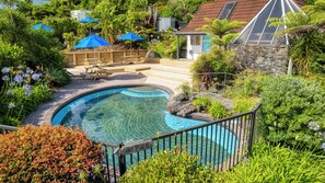 A swimming pool surrounded by lush greenery, with a wooden deck and picnic tables. - The Captains Motel (Russell)