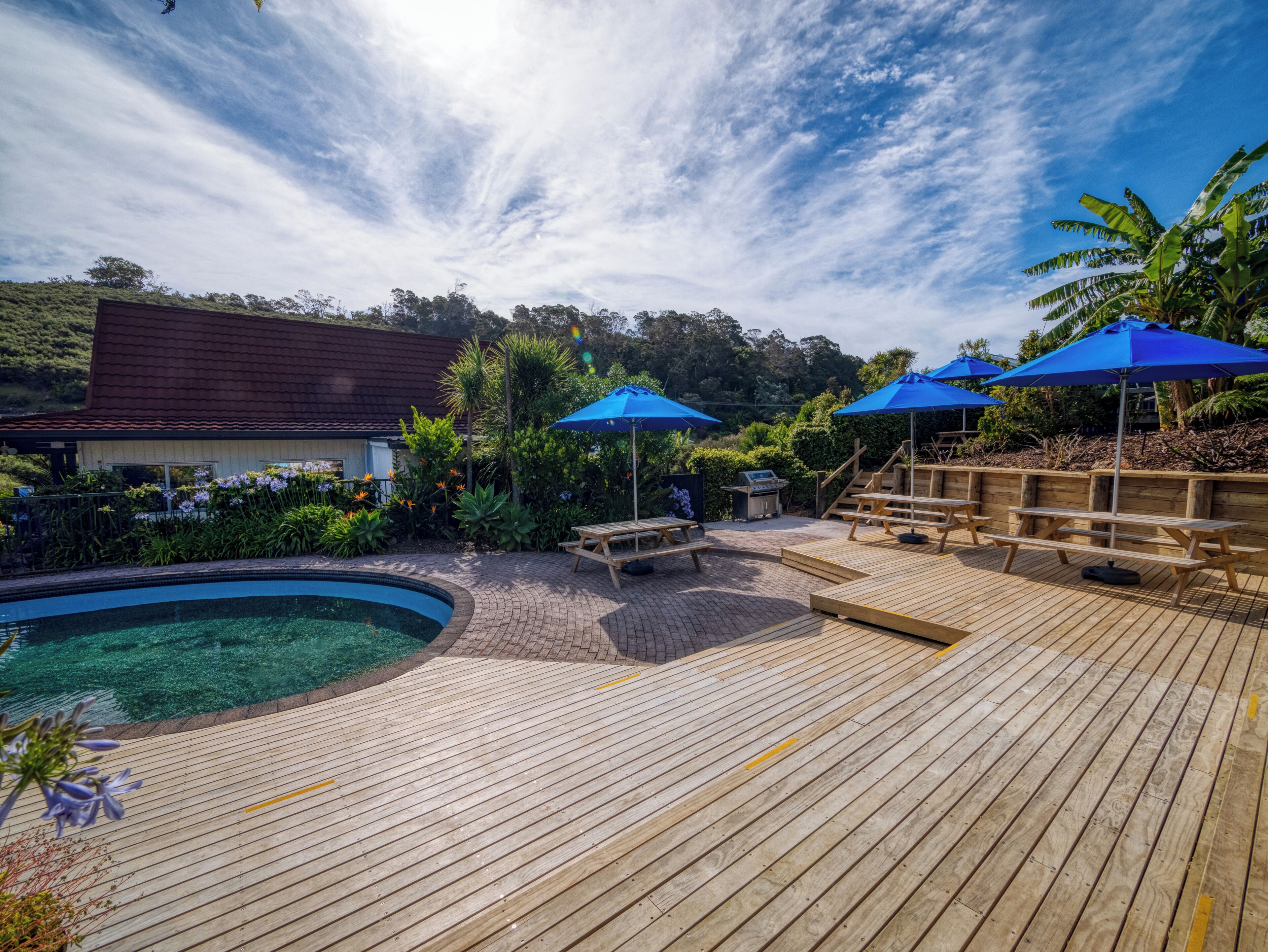 Une terrasse en bois avec une piscine, des sièges d’extérieur et des parasols bleus.