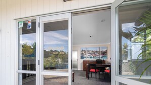 A room with a sliding glass door leading to a patio area. Inside, there is a wooden table with chairs, a painting on the wall, and a view of a harbor through the glass door. - The Captains Motel (Russell)