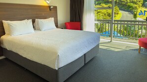 A hotel room with a large bed, a red chair, and a balcony with a view of greenery. - The Captains Motel (Russell)