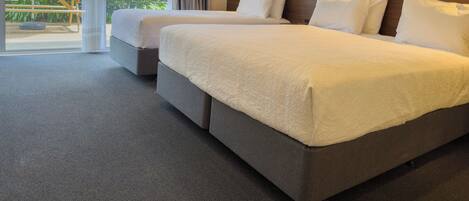Een hotelkamer met twee bedden, een groot raam met gordijnen en uitzicht op groen.