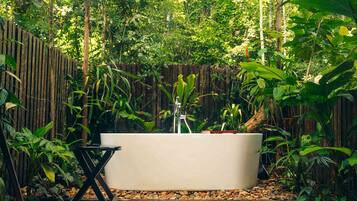 Une baignoire extérieure moderne, entourée d’une végétation luxuriante et d’une clôture en bois.