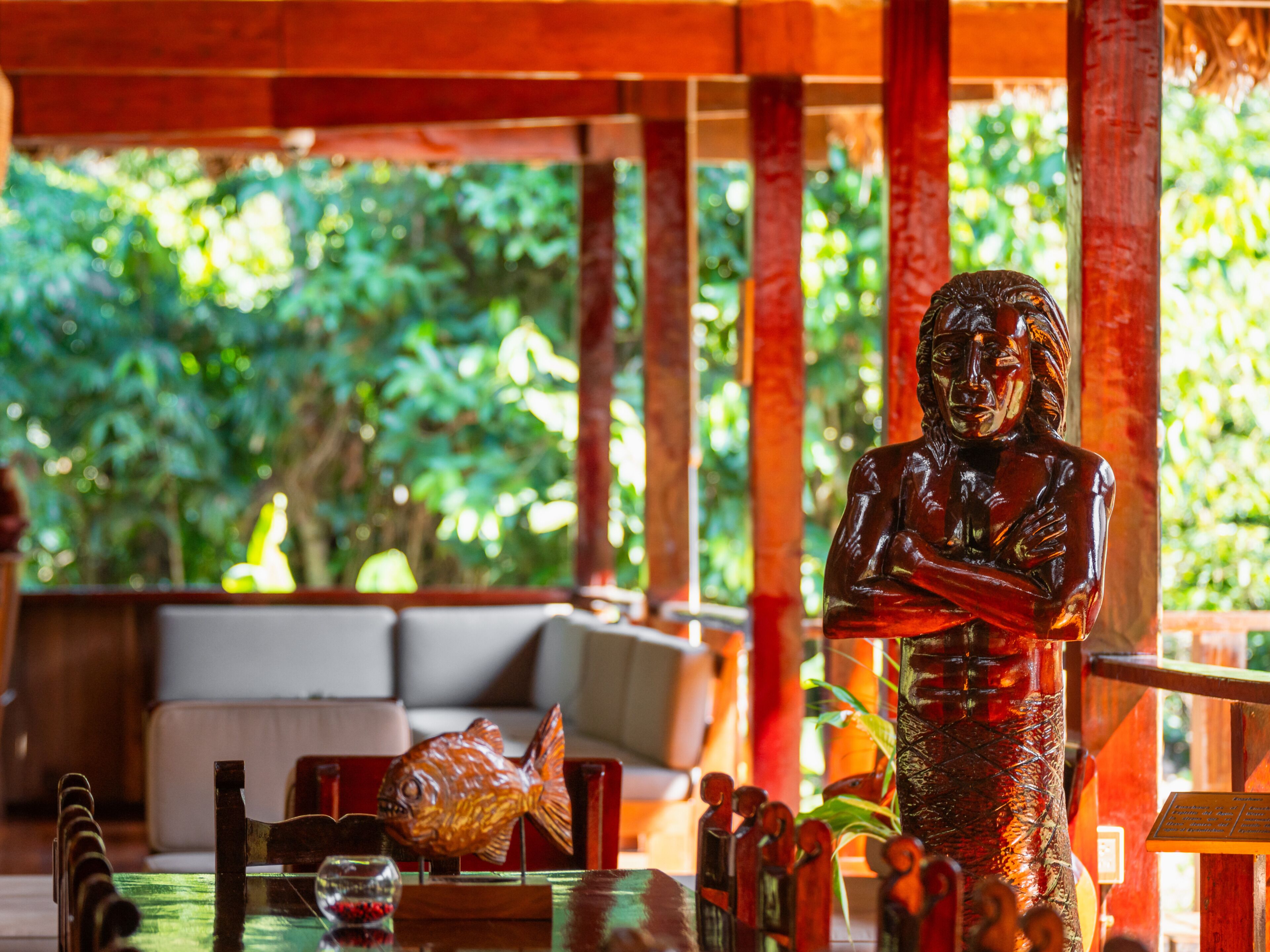 A wooden statue of a seated figure, a fish-shaped object, and a glass container on a table.