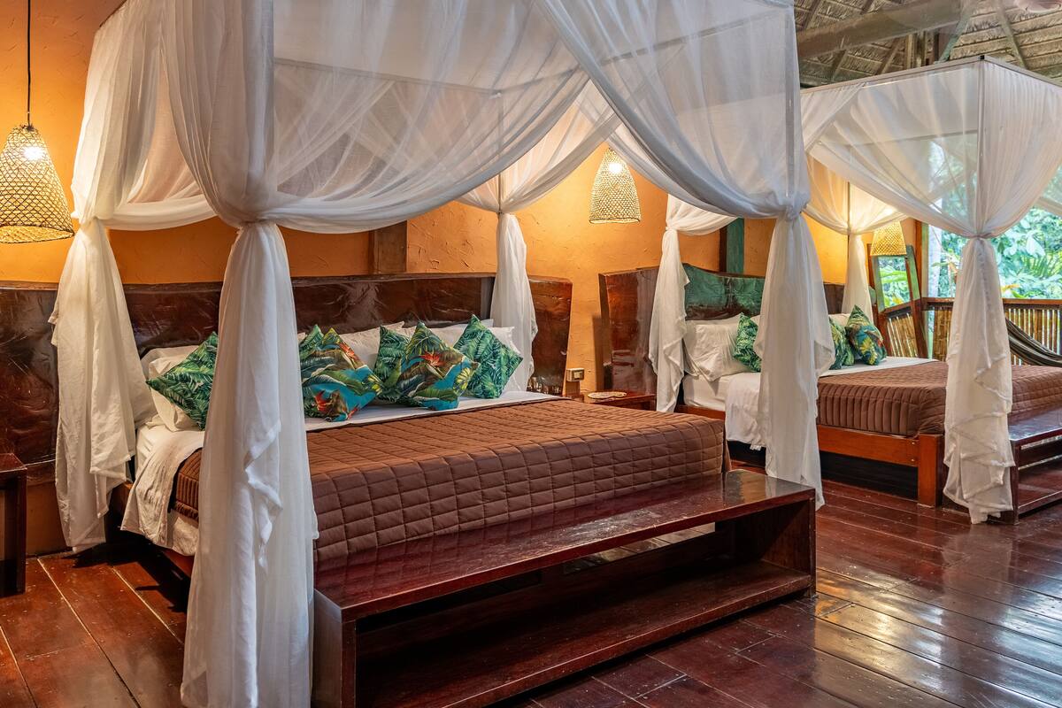 A room with a bed under a canopy, wooden flooring, and a view of the outdoors.