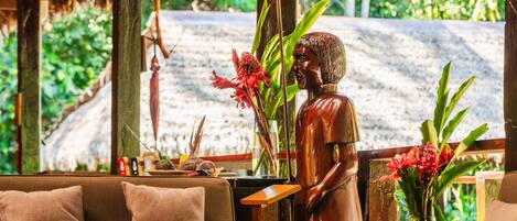 Une statue représentant une personne dans un décor tropical, avec un canapé et une table agrémentée de fleurs.